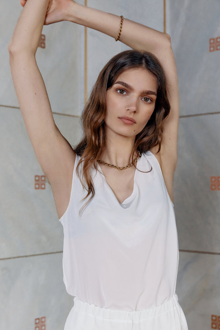 Brunette girl wearing sleeveless silk top Anonymo in white color alternative close up view with raised hands